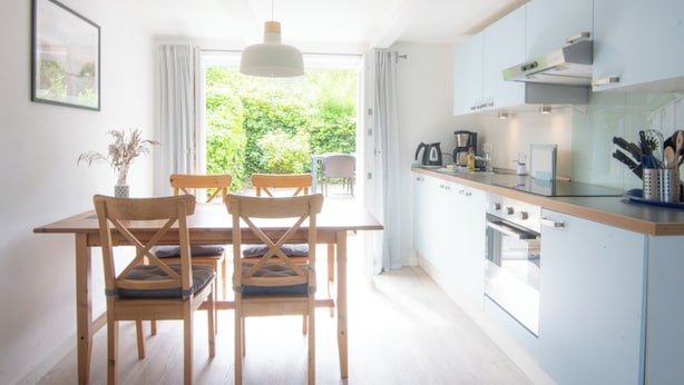 Et moderne køkken med træstole, et spisebord og udsigt til grønne omgivelser.