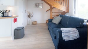 Et moderne interiør med et køkkenområde, en trappe i træ, en blå sofa og et vindue.