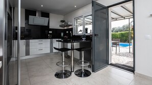 A modern kitchen with a black countertop, stainless steel bar stools, and a large window overlooking a pool. - Charming Villa with Private Pool (4V4) (Altura)