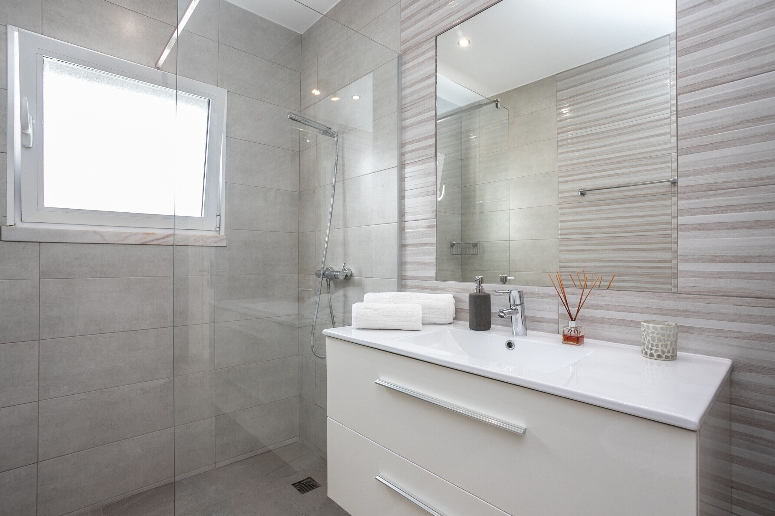 A modern bathroom with a glass shower enclosure, a large mirror, and a white vanity with a sink.