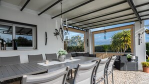 An outdoor patio with a dining table and chairs, a hanging light fixture, and a view of the garden. - Charming Villa with Private Pool (4V4) (Altura)
