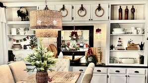 A cozy dining area with a wooden table and chairs, surrounded by white cabinetry and shelves with various kitchen items.