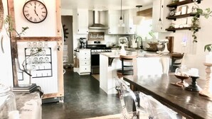 A modern kitchen with white cabinets, a central island, and a dining area with clear chairs.