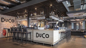Een bar met een bakstenen muur, barstoelen en flessen en glazen op planken.