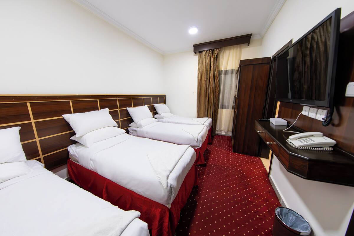Ein Hotelzimmer mit drei Betten, einem Fernseher, einem Telefon und einem Mülleimer.