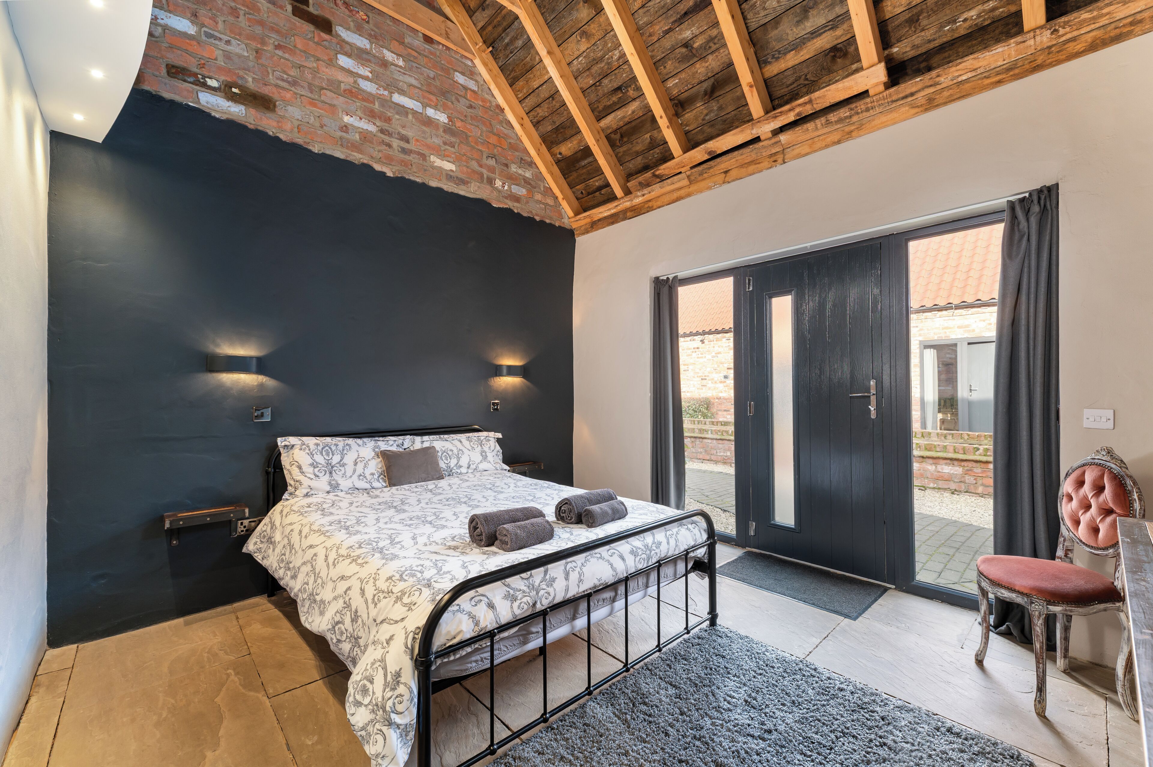 A bedroom with a bed, a chair, a door, and a view of the outside.