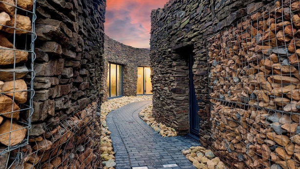 A stone-walled corridor with a curved brick pathway, metal fencing, and a door leading to a room with a view. - Chapel Farm Hotel (Wellow)
