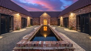 A brick building with a central courtyard, a reflective water feature, and a sunset sky. - Chapel Farm Hotel (Wellow)