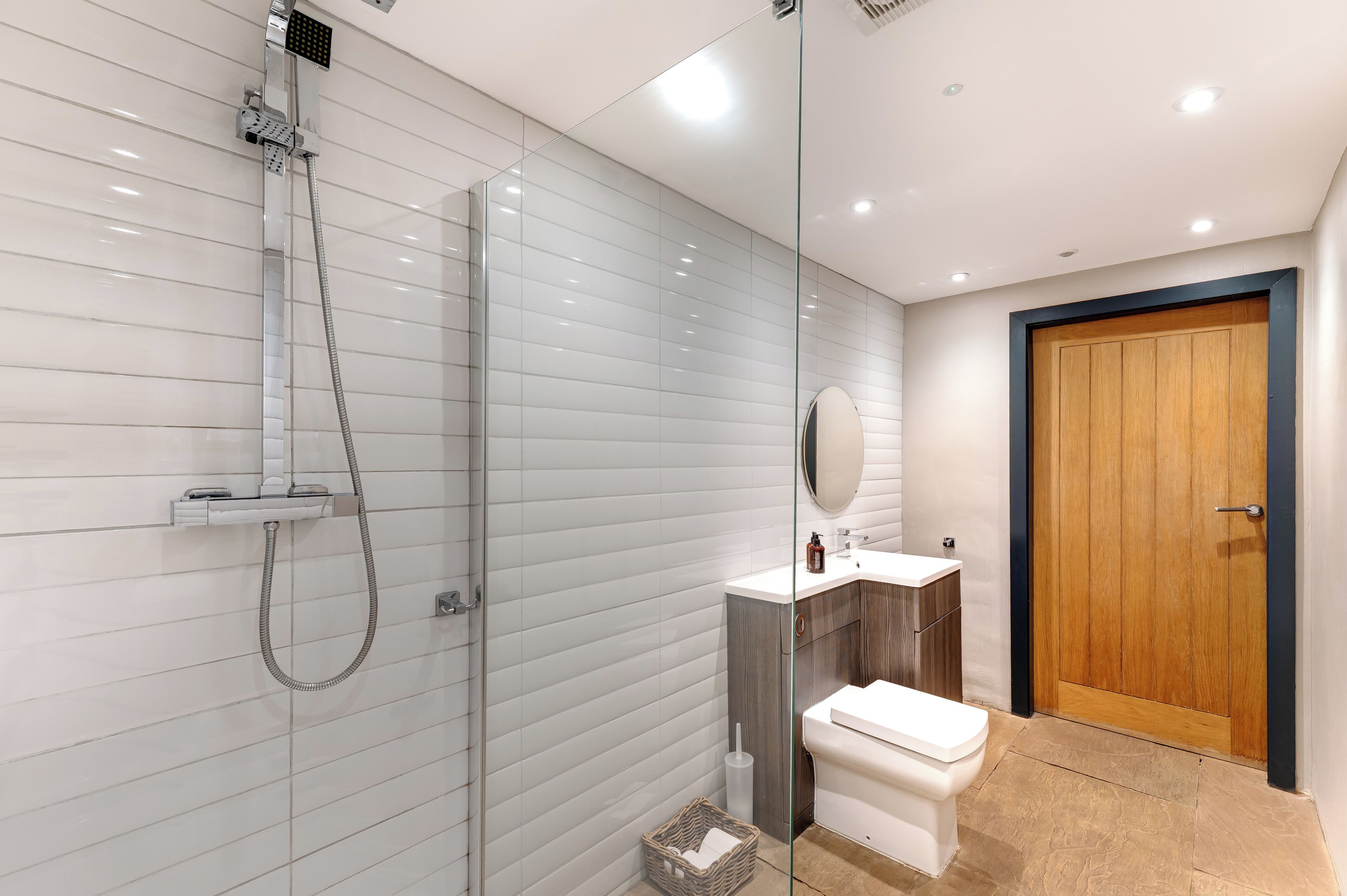 A modern bathroom with a glass-enclosed shower, a wooden door, and a white toilet.