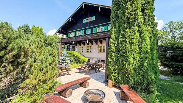 Un edificio de estilo chalet con terraza de madera, mesas de picnic y una zona de fuego.