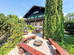 Un edificio de estilo chalet con terraza de madera, mesas de picnic y una zona de fuego.