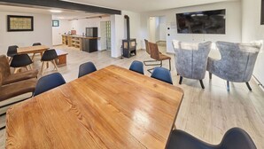 Una sala de estar moderna con una mesa de comedor de madera, sillas azules y grises, una chimenea y un televisor de pantalla plana montado en la pared.
