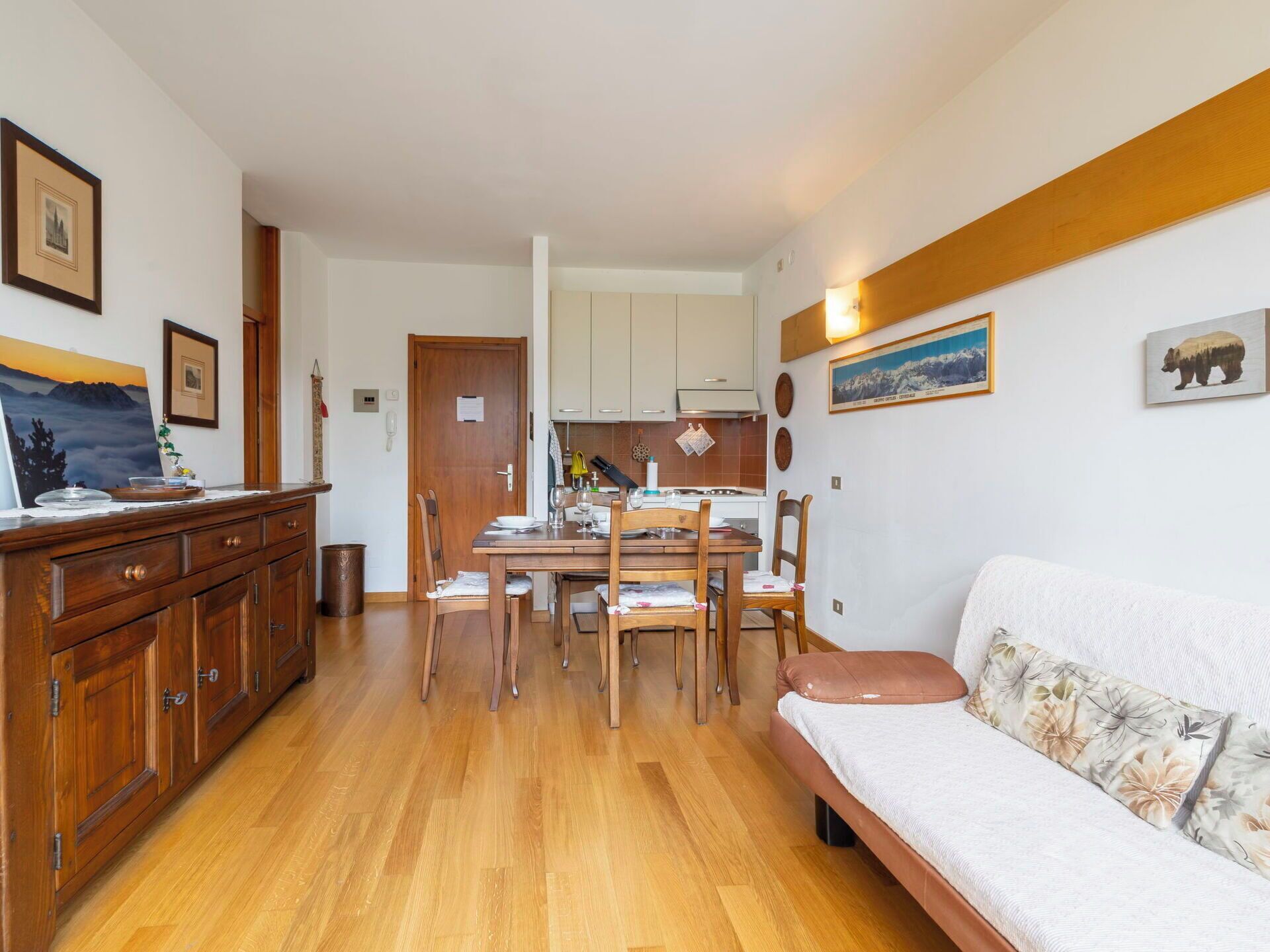 Un comedor con mesa y sillas de madera, un sofá y una cocina al fondo.