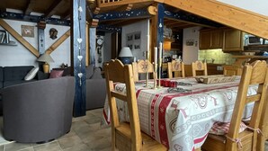 A cozy room with a wooden dining table set for four, a sofa, and a large window. - Large triplex at the foot of the slopes ideal for two families (Morillon)