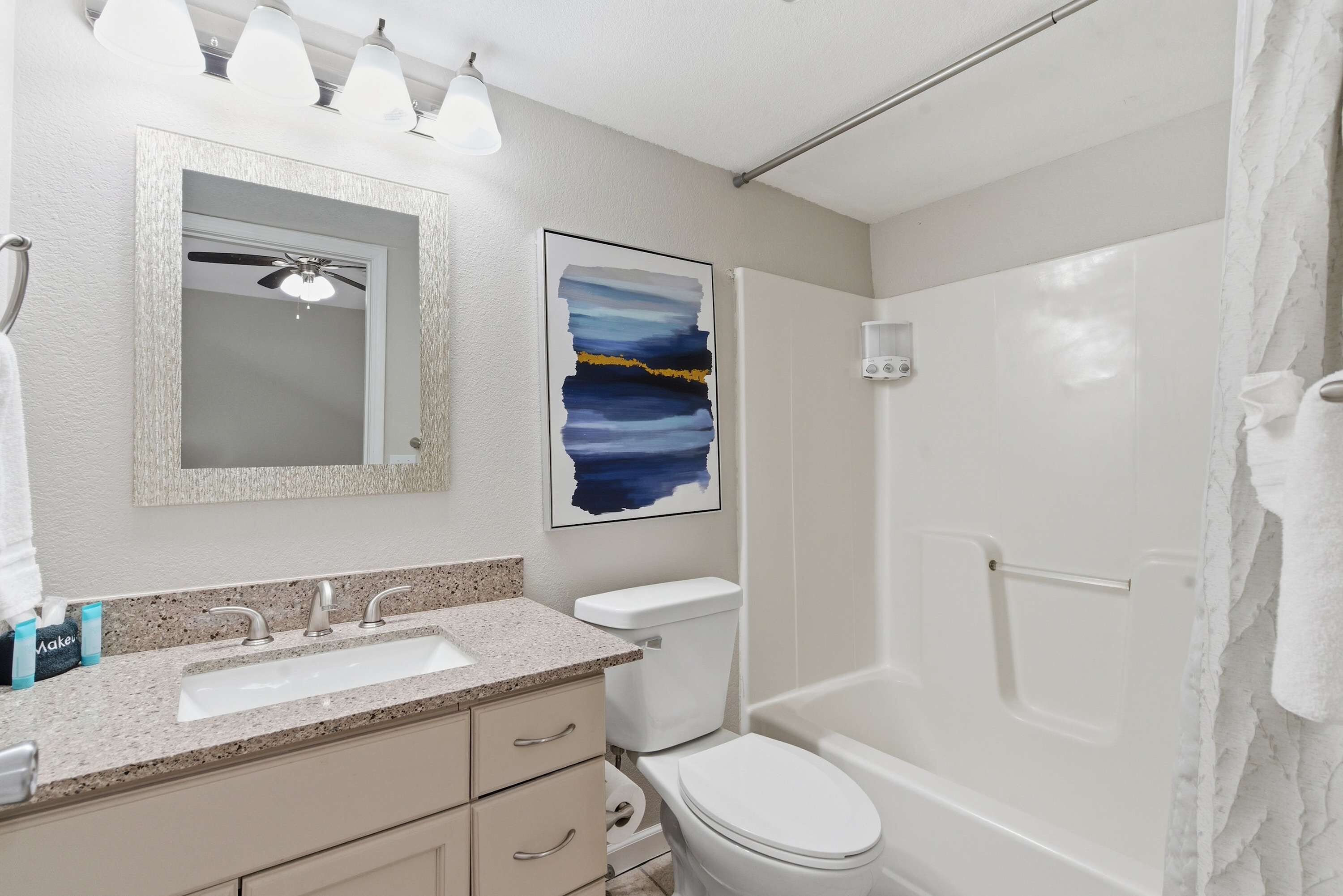 A bathroom with a sink, mirror, ceiling fan, toilet, and shower.