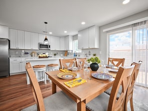A modern kitchen with white cabinets, a wooden dining table, and a large window. - New 2025 Modern Home, Ice-Cold A/C, 8 Min to Sky Harbor, Sleeps 6 (Phoenix)