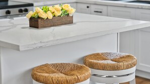 Eine Küche mit Marmorarbeitsplatte, einer Holz-Blumendekoration und zwei Korbstühlen.