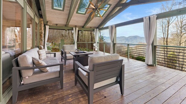 Ein überdachter Außenbereich mit Holzdeck, gepolsterten Sitzgelegenheiten und Blick auf die Berge.