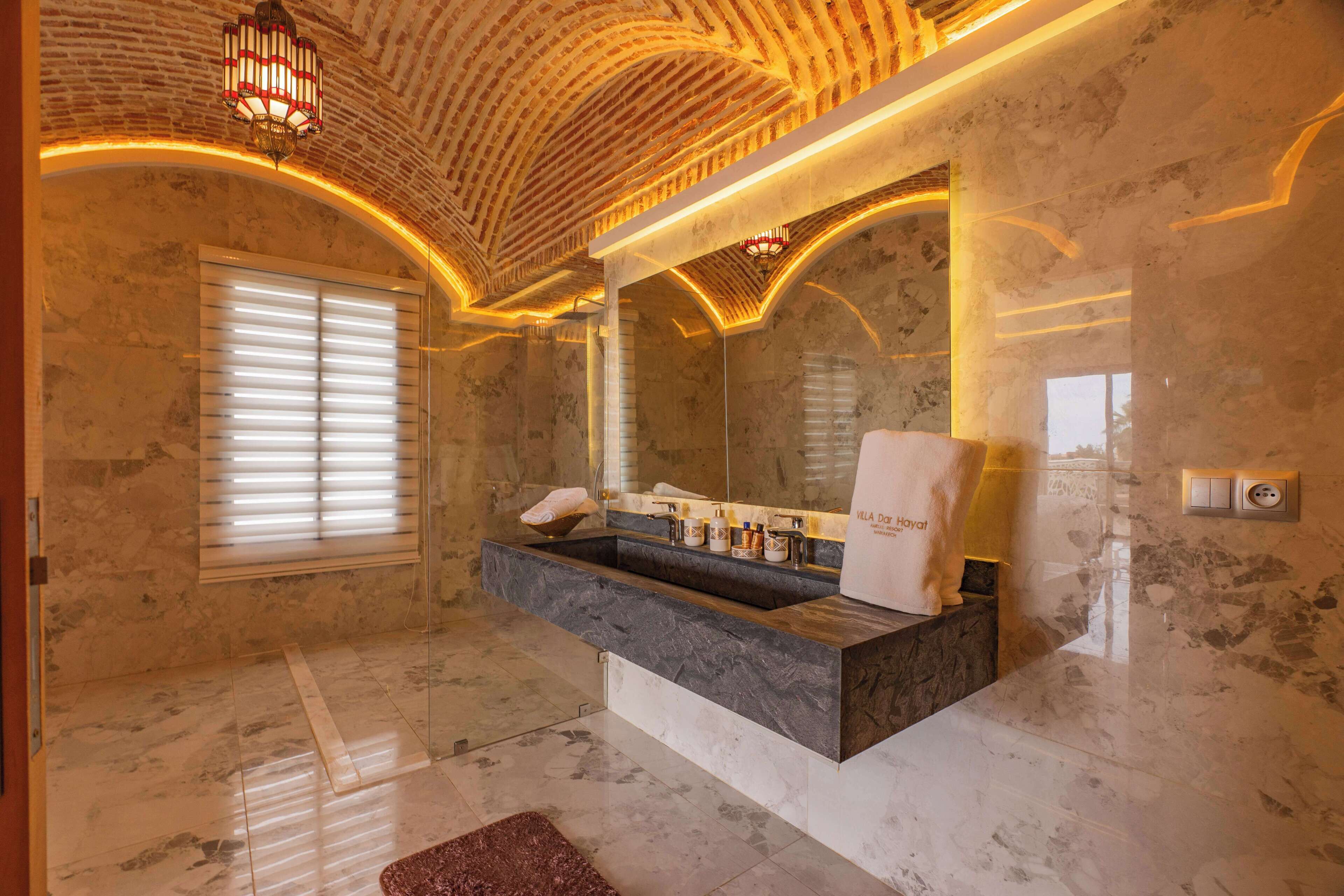 A bathroom with a marble sink, a large mirror, and a ceiling with a unique brick pattern.