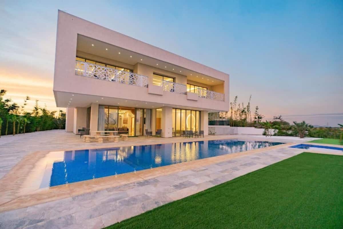 A modern two-story house with a swimming pool, large windows, and a well-maintained lawn.