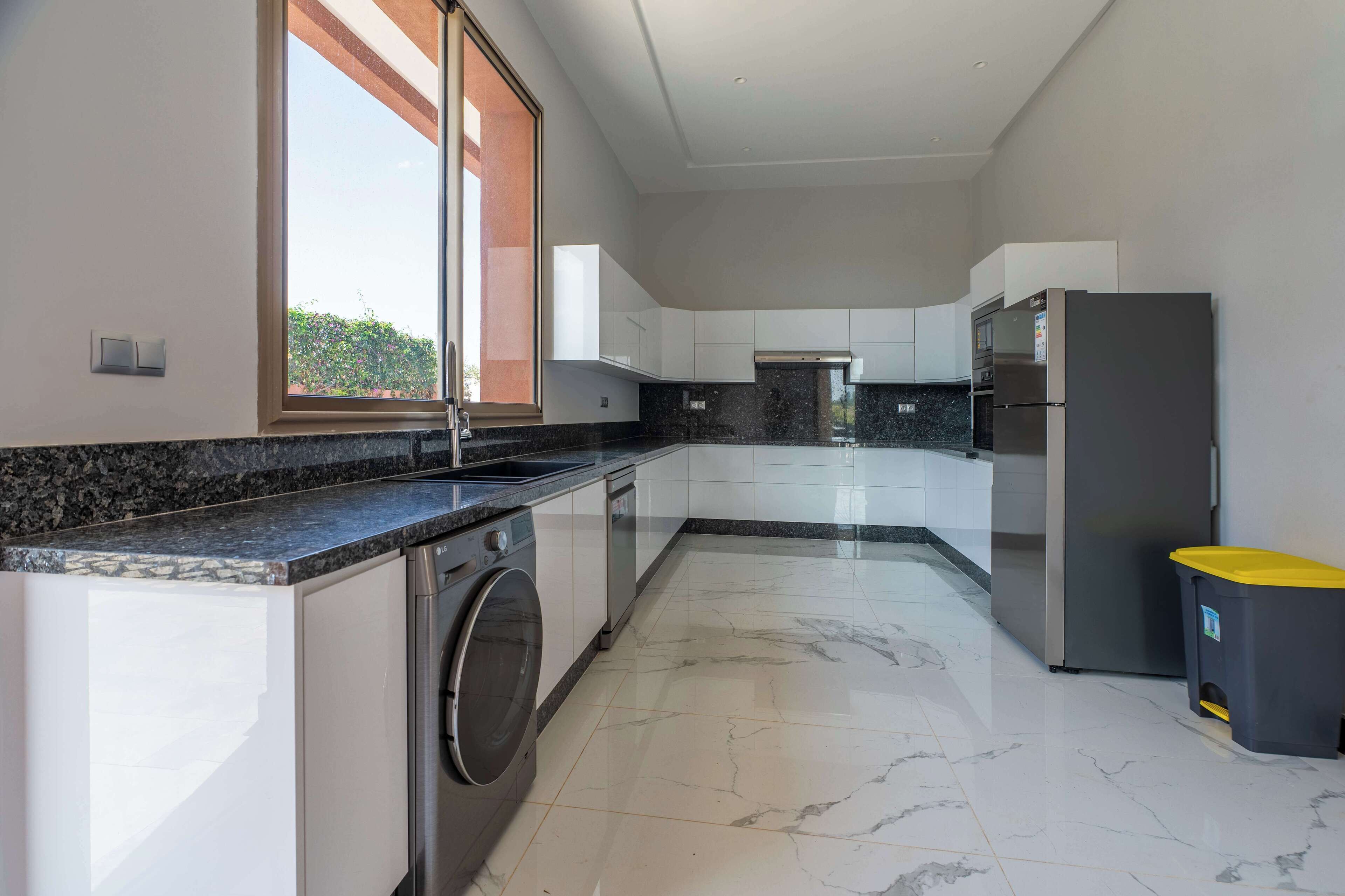A modern kitchen with a washing machine, a refrigerator, and a trash bin.