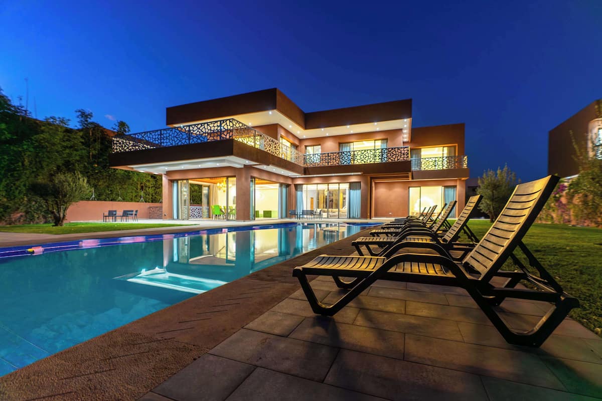 A modern hotel with a swimming pool, outdoor seating, and a well-lit exterior at dusk.