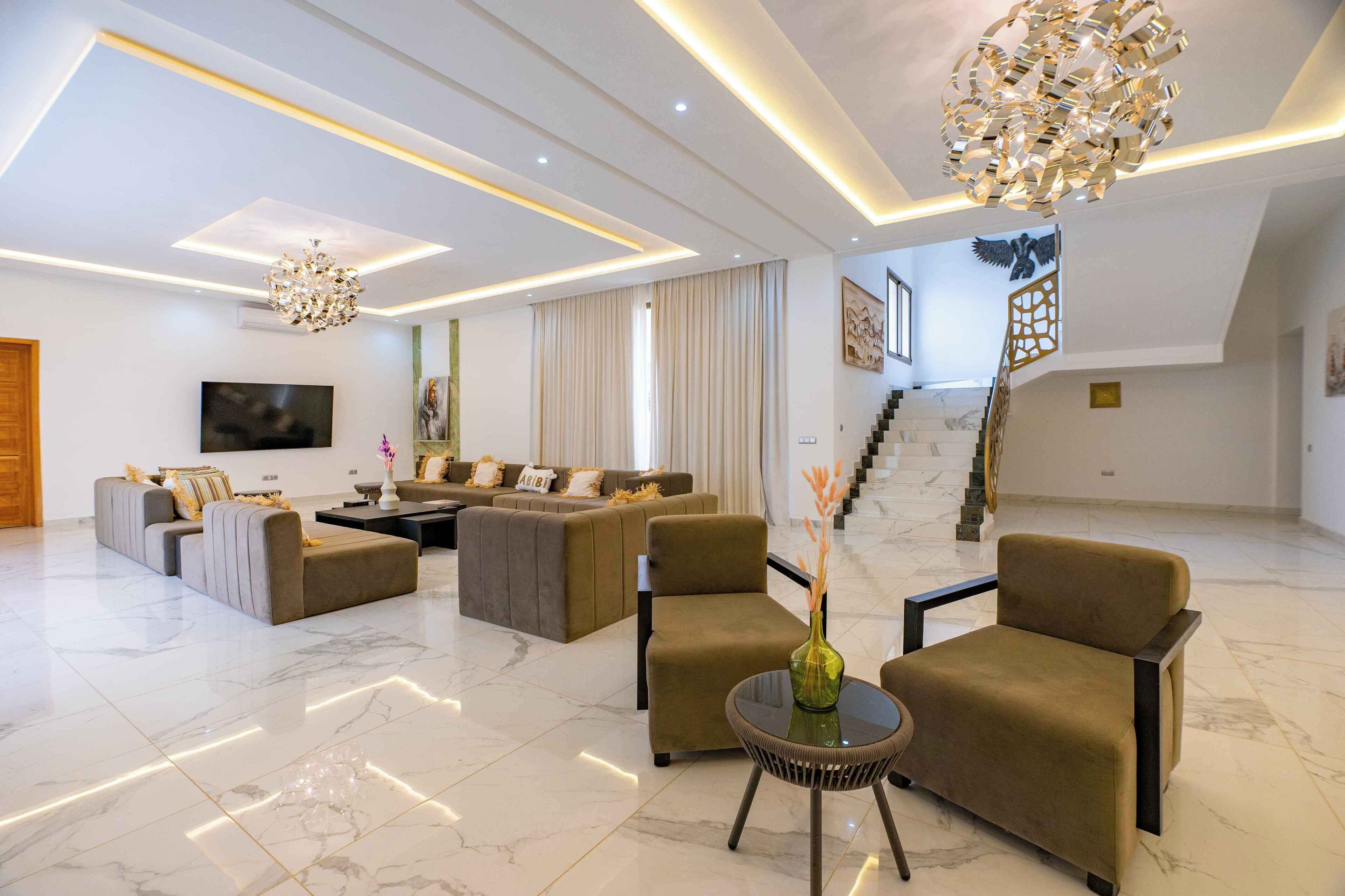 A spacious living area with a modern chandelier, a staircase, and a flat-screen TV.