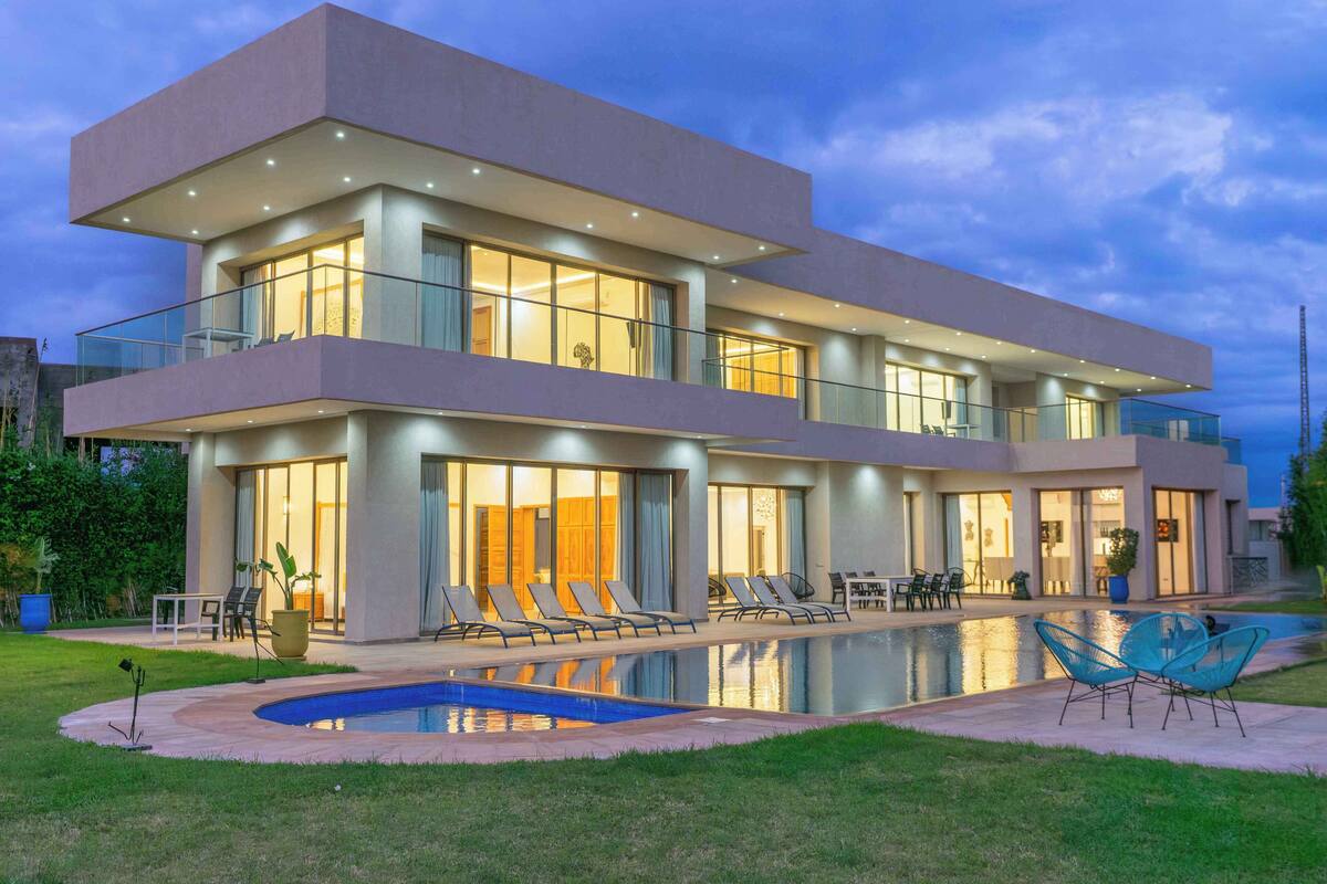 A modern two-story house with a swimming pool, outdoor seating, and large windows.