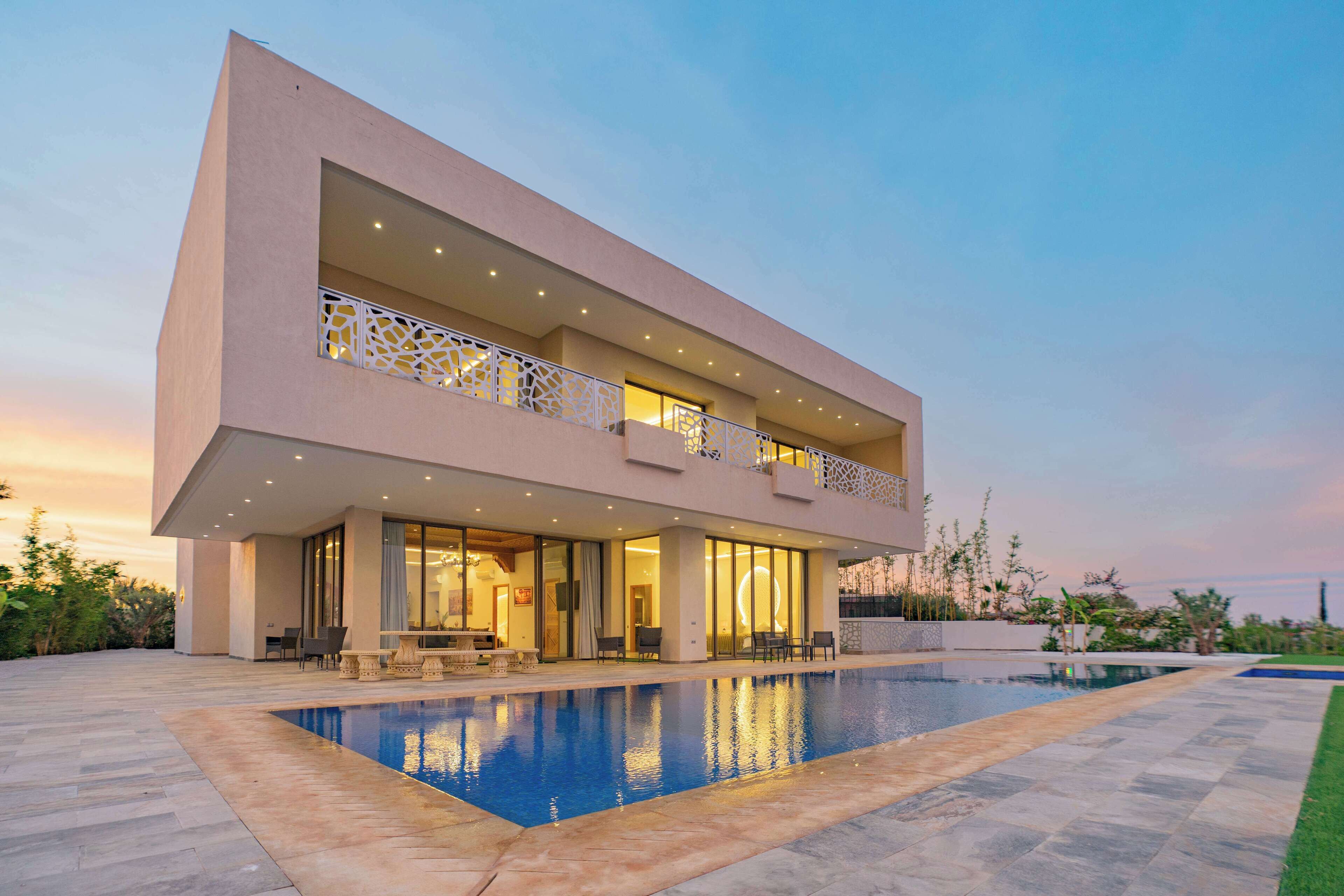 A modern two-story house with a swimming pool, outdoor seating, and a well-lit balcony.