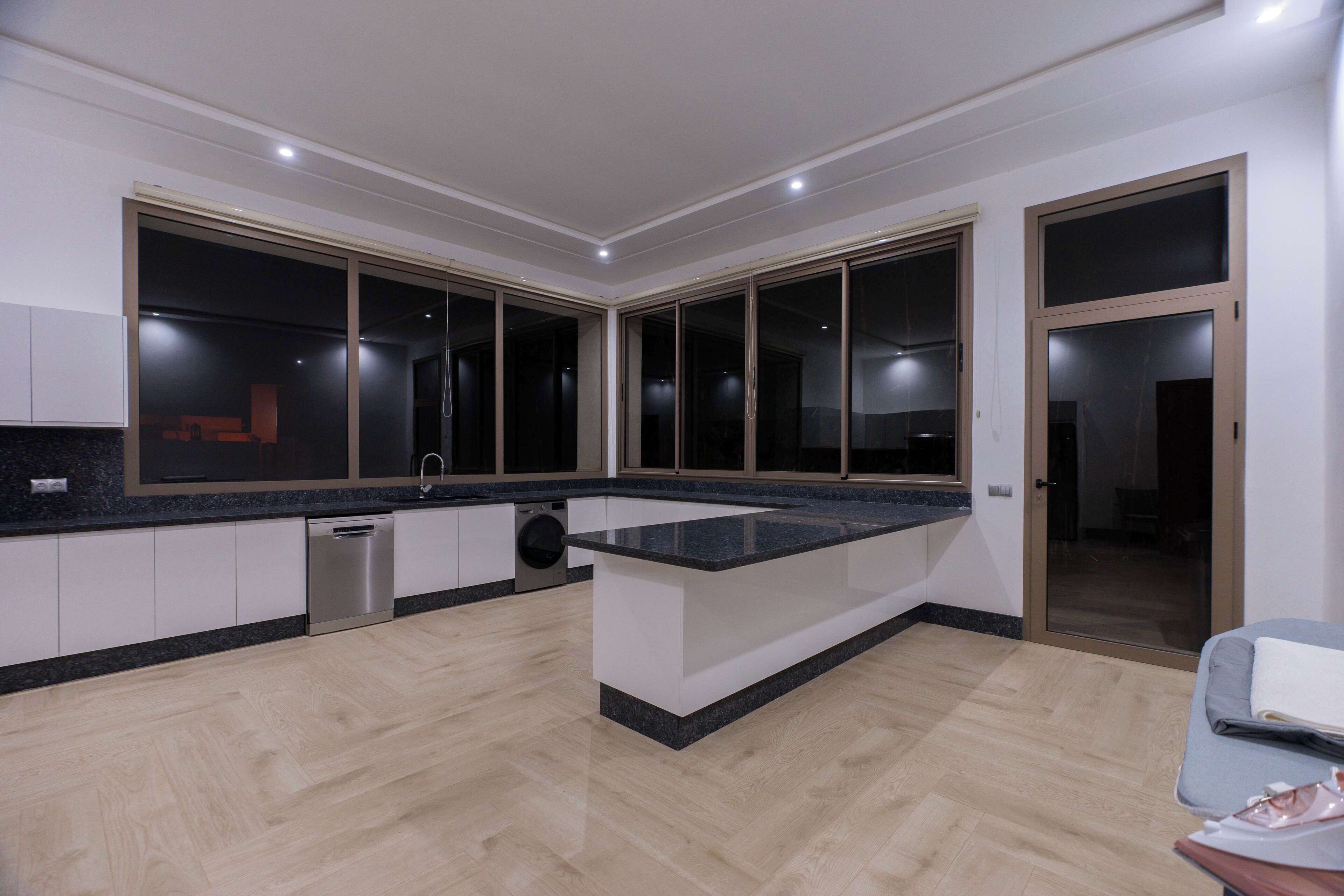 Una cocina moderna con una isla central, electrodomésticos integrados y amplios ventanales.
