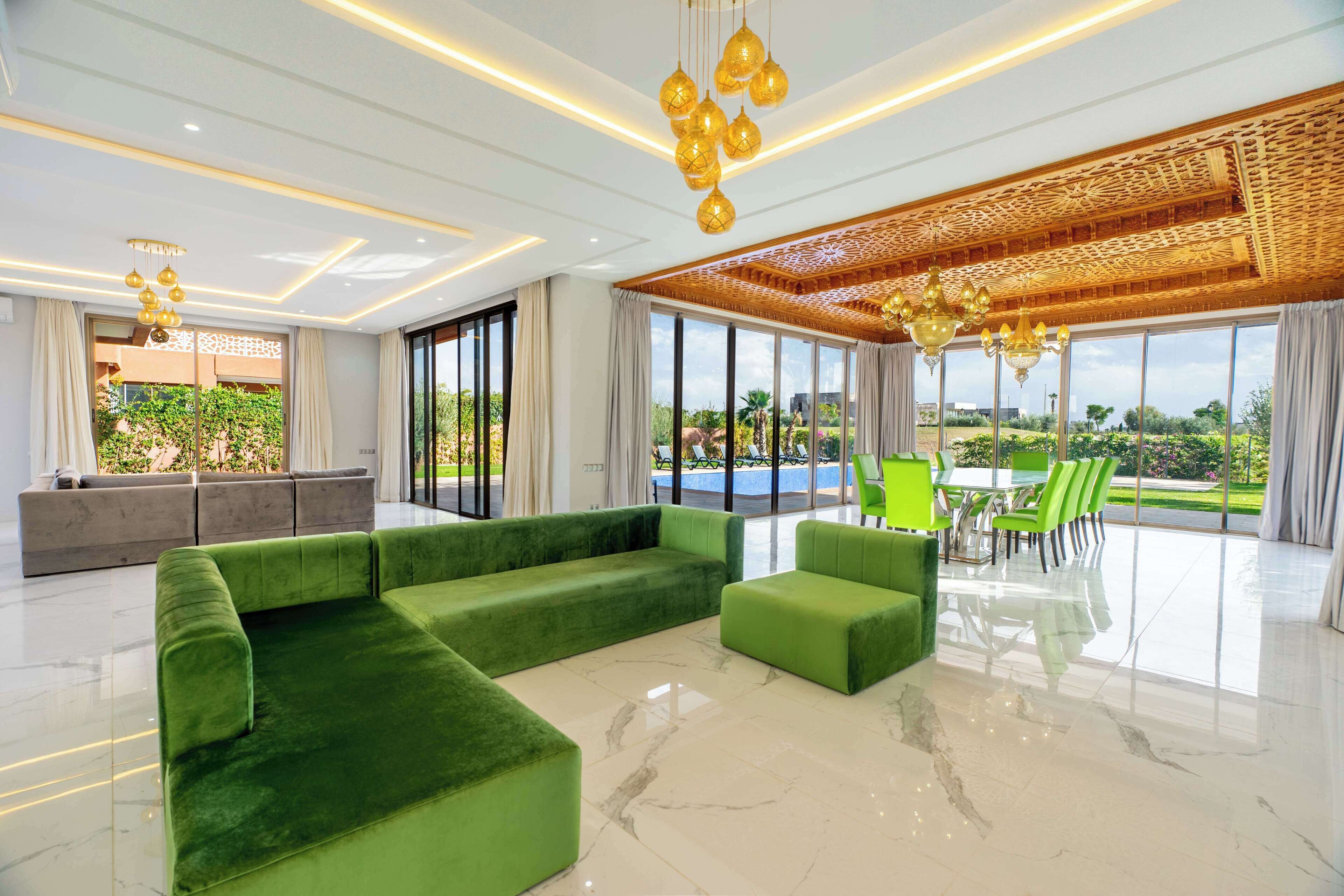 Un vaste espace de vie comprenant un canapé vert, une table à manger avec des chaises et une vue sur l’extérieur.