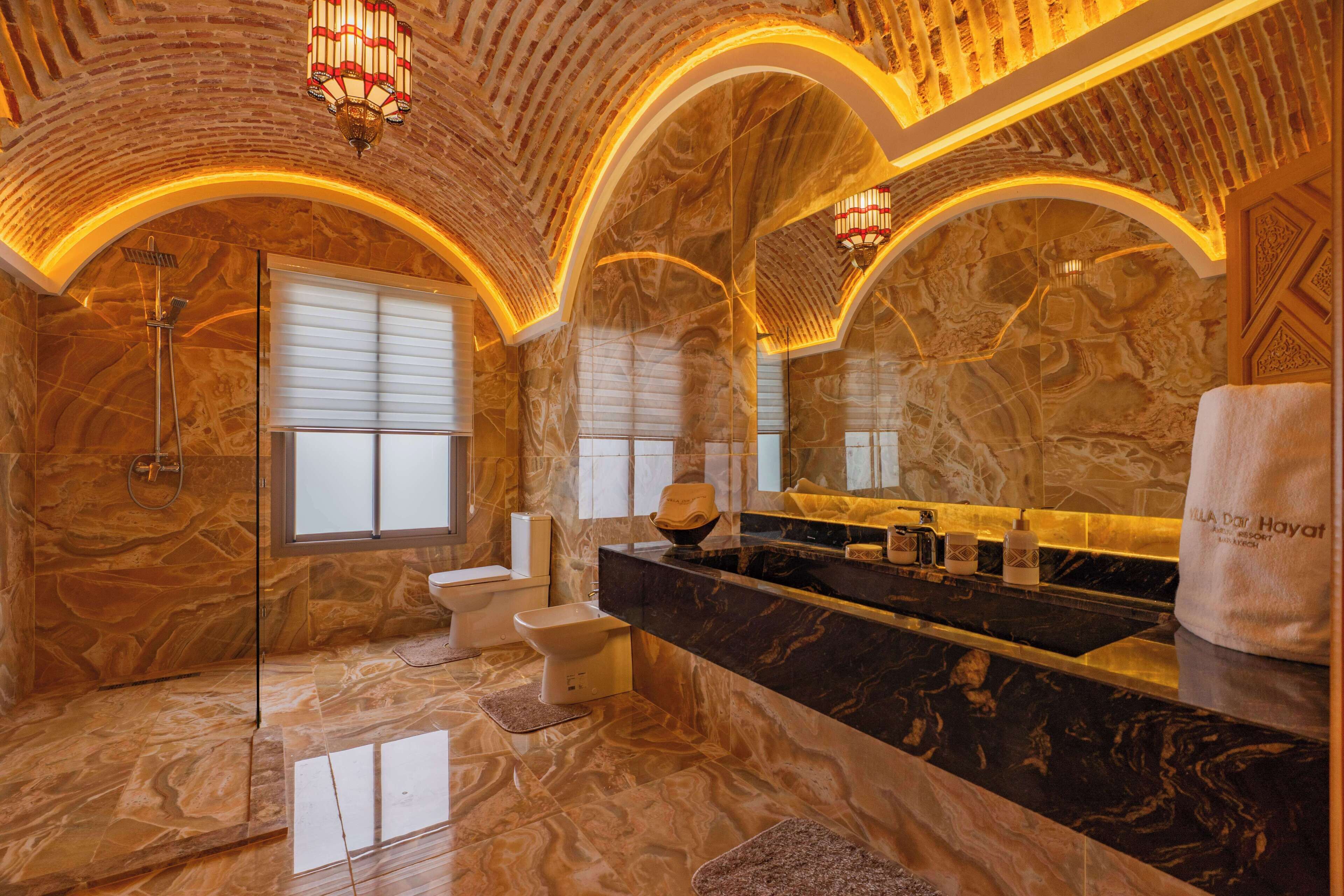 A luxurious bathroom with marble walls, a black marble vanity, a glass shower enclosure, and a large mirror.