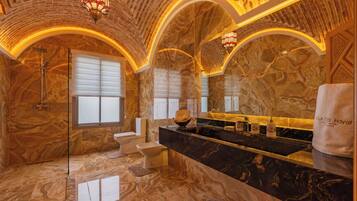 A luxurious bathroom with marble walls, a black marble vanity, a glass shower enclosure, and a large mirror.