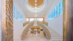 Eine prachtvolle Treppe mit aufwendigen goldfarbenen Geländern führt zu einer großzügigen Lobby mit hoher Decke und einem zentralen Kronleuchter.