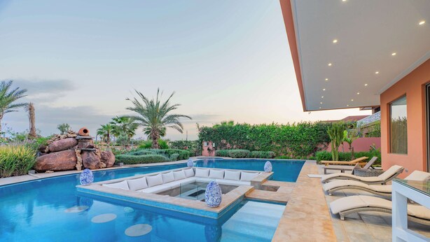 Ein moderner Poolbereich im Freien mit integriertem Sitzbereich, Liegestühlen und Blick auf die umliegende Landschaft.