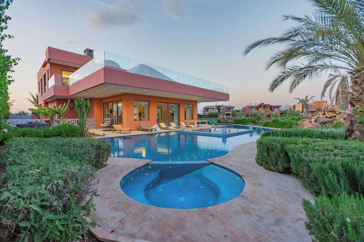 A modern house with a swimming pool, surrounded by greenery and palm trees.