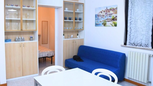 Ein Zimmer mit einem blauen Sofa, weißen Stühlen, einem weißen Tisch und Holzschränken mit Glastüren.