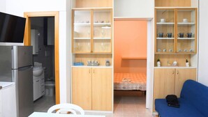 Ein kompaktes Zimmer mit Küchenzeile, einem Bett, einem blauen Schlafsofa und Einbauschränken mit Regalen.