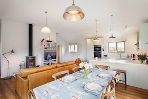 A modern living space with a dining area, kitchen, and a fireplace. - Sloopside - Bantham, South Devon (Bantham)