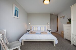 Quarto com cama, mesas de cabeceira, uma cadeira, cômoda e um quadro na parede.
