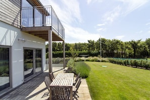 A modern building with a balcony, a patio with wooden furniture, and a well-maintained lawn. - Sloopside - Bantham, South Devon (Bantham)