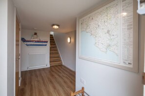 Un couloir doté d’un plancher en bois, d’un radiateur blanc, d’une carte encadrée accrochée au mur et d’un escalier menant à un autre niveau.