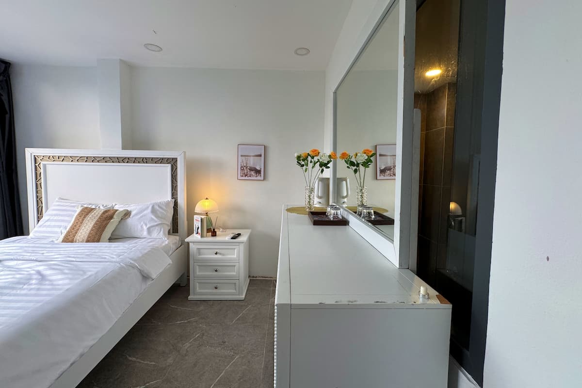 A hotel room with a bed, bedside table, lamp, and a mirror.