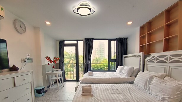 A hotel room with two beds, a desk, a dresser, a TV, and a balcony with curtains. - Came House - Near Bui Vien street (Ho Chi Minh City)