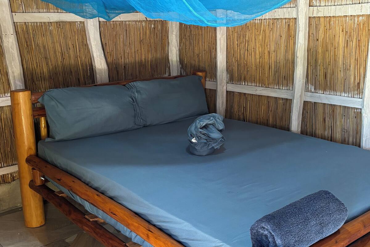 Una cama con colchón azul, estructura de madera y mosquitero.