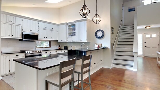 A modern kitchen with white cabinets, a central island, a microwave, stove, and hanging pendant lights. - Sandstorm-New '26, Pet Friendly Home with Outdoor Space (Pawleys Island)