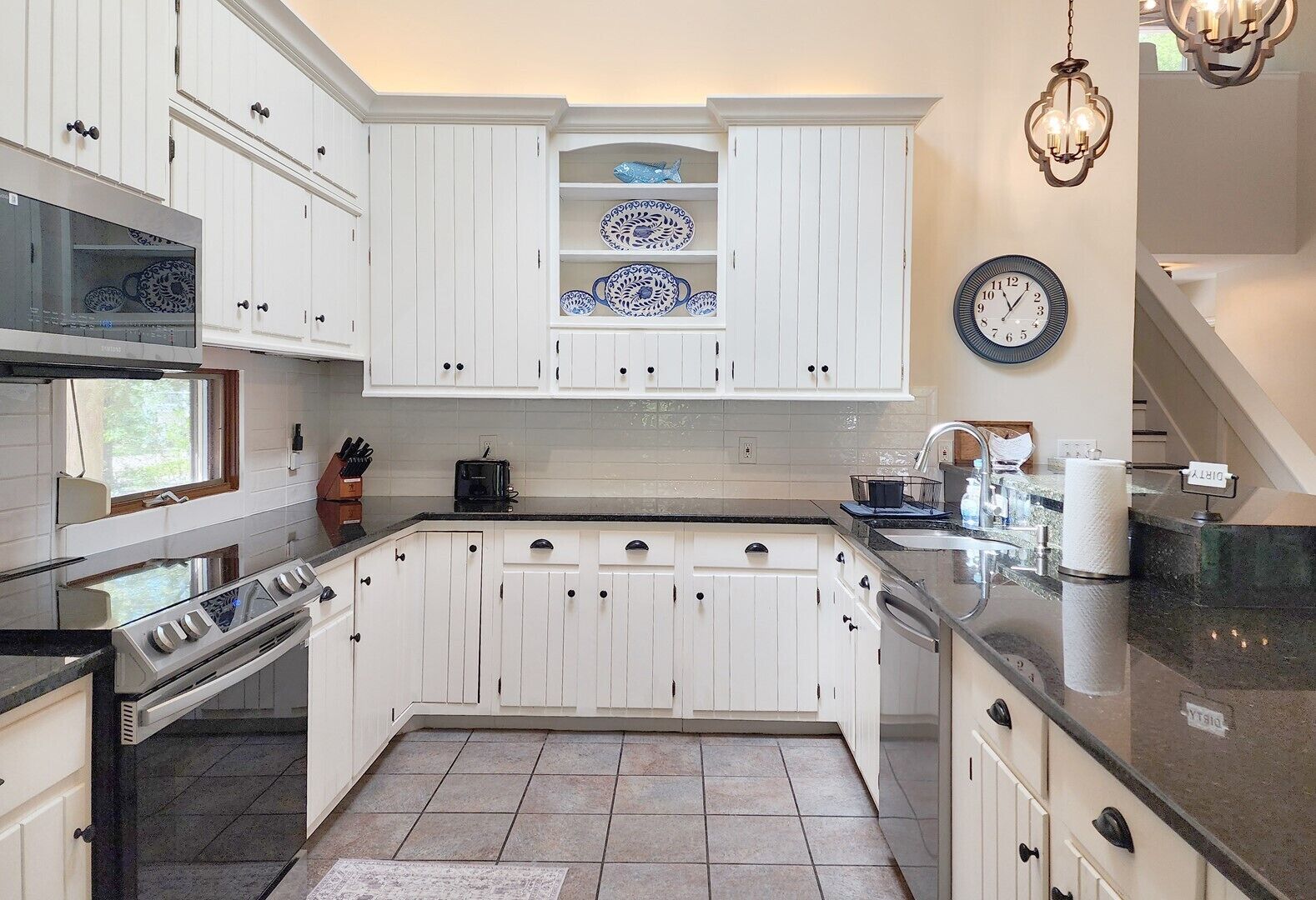 A kitchen with white cabinetry, a stove, a sink, and a clock on the wall.