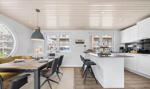 A modern kitchen with white cabinetry, a central island, and a dining area with a table and chairs. - Wasserhaus im Pionierhafen - Washing Machine, Roof Terrace, TV, Parking Space (Schleswig)