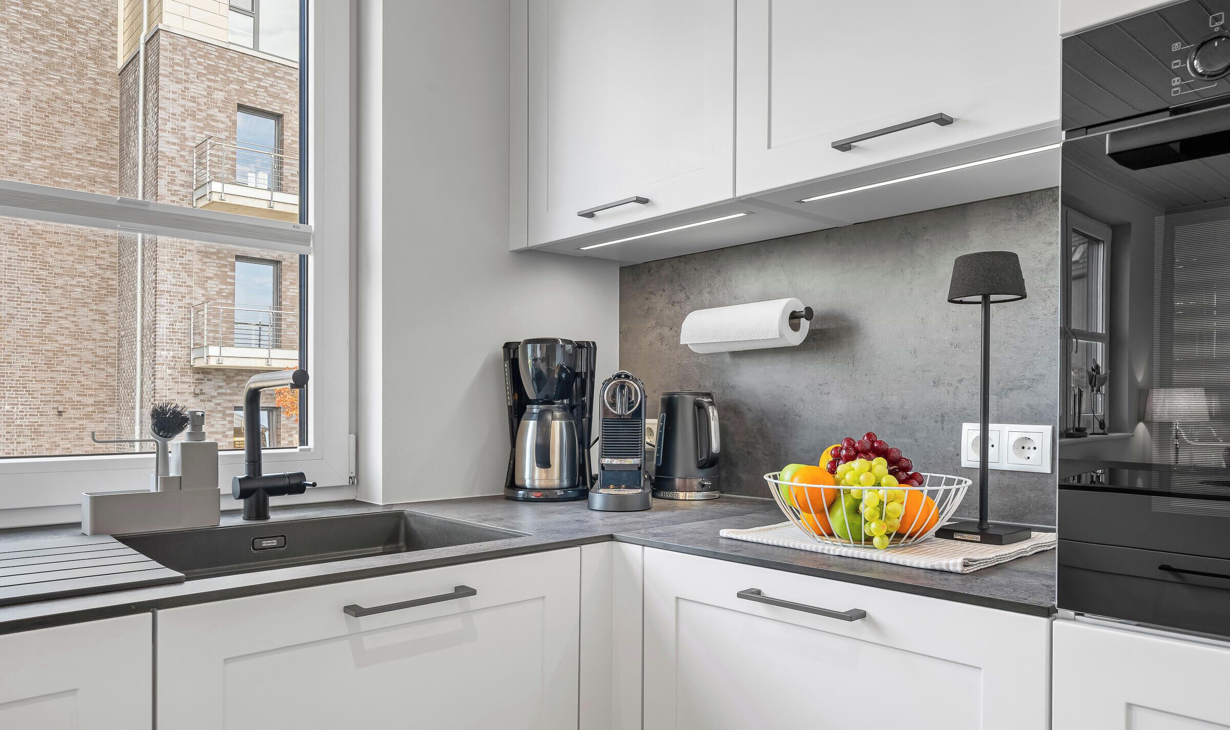 Una cocina moderna con un lavamanos integrado, una cafetera, un hervidor y un frutero sobre la encimera.