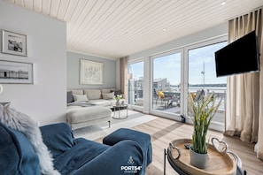 A modern living room with a sofa, a coffee table, and a TV. There is a balcony with a view of the city. - Wasserhaus im Pionierhafen - Washing Machine, Roof Terrace, TV, Parking Space (Schleswig)